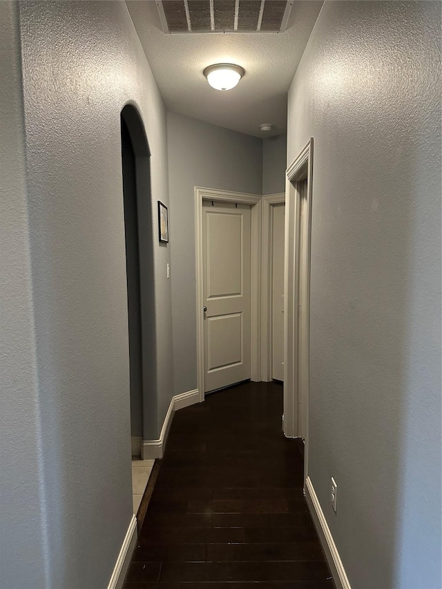 corridor with a textured ceiling, dark wood finished floors, visible vents, and baseboards