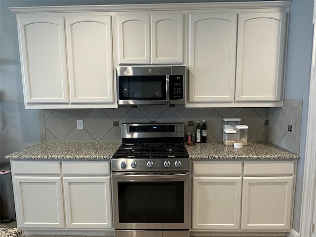 kitchen with stainless steel appliances, backsplash, white cabinetry, and light stone countertops