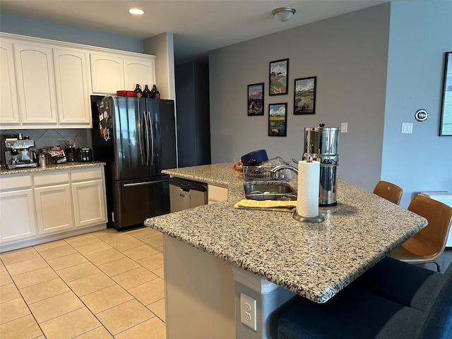 kitchen featuring a breakfast bar area, a sink, white cabinets, stainless steel dishwasher, and freestanding refrigerator