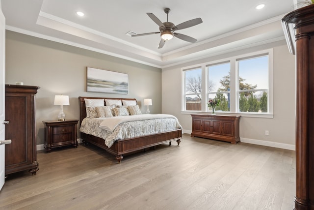 bedroom with a raised ceiling, crown molding, light wood-style flooring, and baseboards