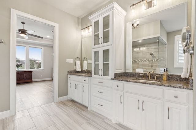 full bath with double vanity, ceiling fan, a sink, a shower stall, and baseboards