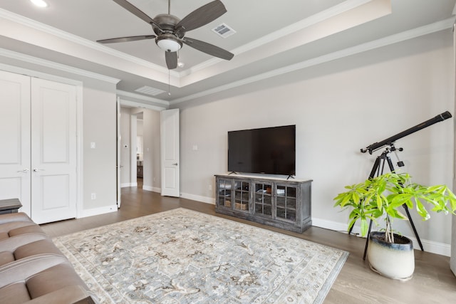 living area featuring baseboards, visible vents, wood finished floors, a tray ceiling, and crown molding