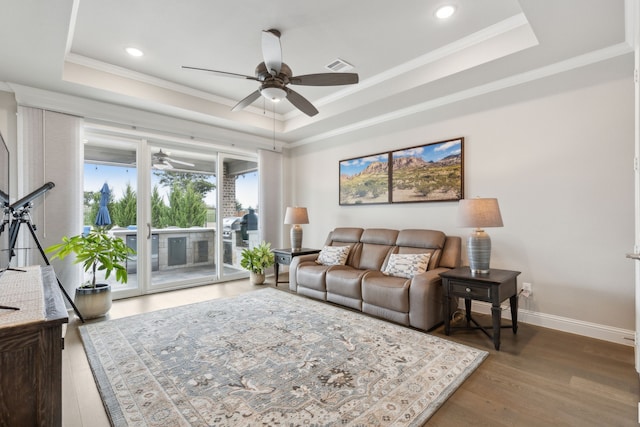 living room with baseboards, a tray ceiling, and crown molding