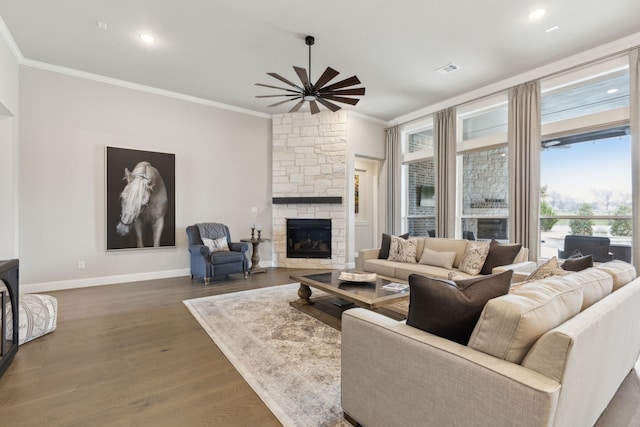 living room featuring crown molding, dark wood finished floors, ceiling fan, a stone fireplace, and baseboards