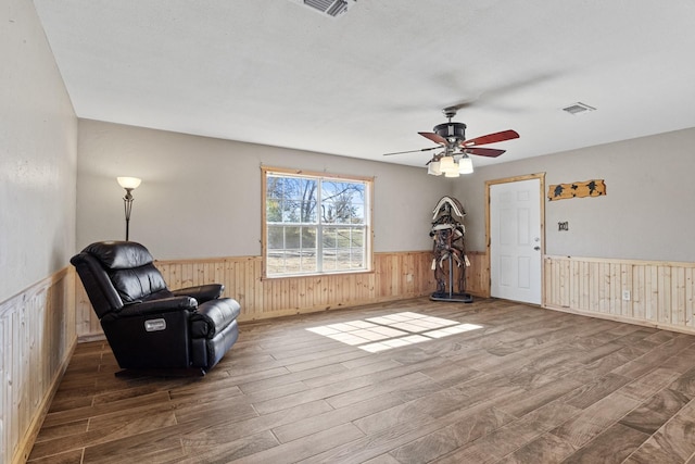 living area with a wainscoted wall, visible vents, wood finished floors, and wood walls