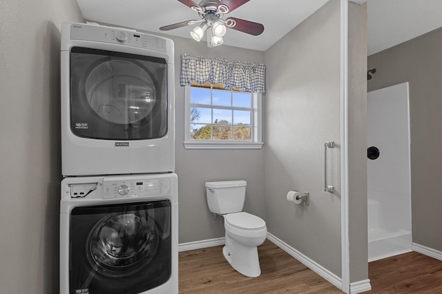 full bathroom with a shower, stacked washer and dryer, toilet, wood finished floors, and baseboards