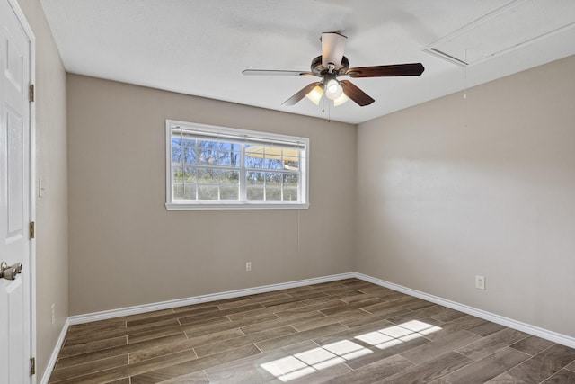 spare room featuring attic access, a ceiling fan, baseboards, and wood finished floors