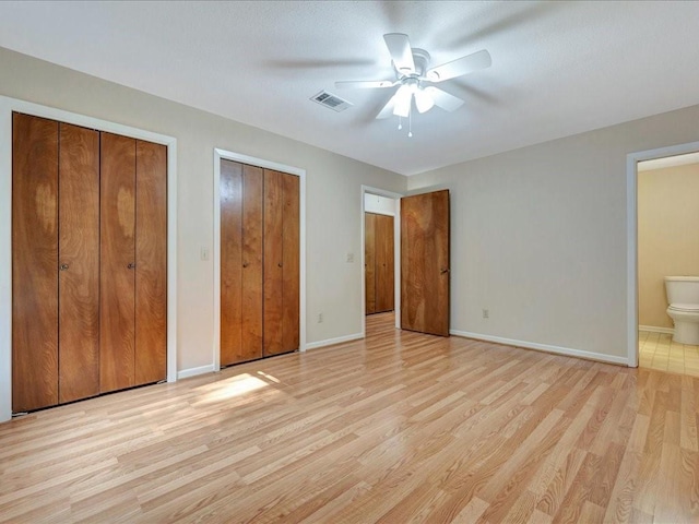 unfurnished bedroom featuring baseboards, visible vents, connected bathroom, light wood-type flooring, and two closets