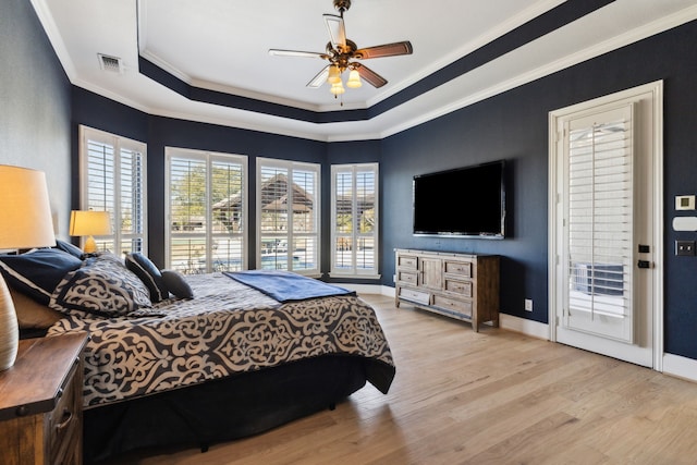 bedroom with a tray ceiling, baseboards, crown molding, and light wood finished floors