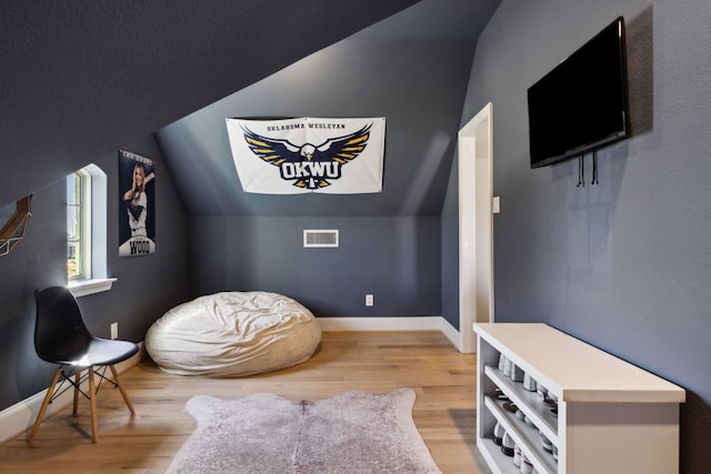 living area featuring light wood finished floors, baseboards, visible vents, and vaulted ceiling