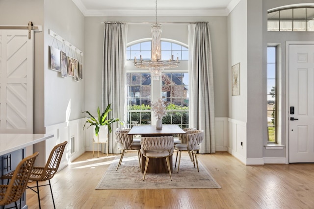 dining area with crown molding, a barn door, light wood-type flooring, and an inviting chandelier