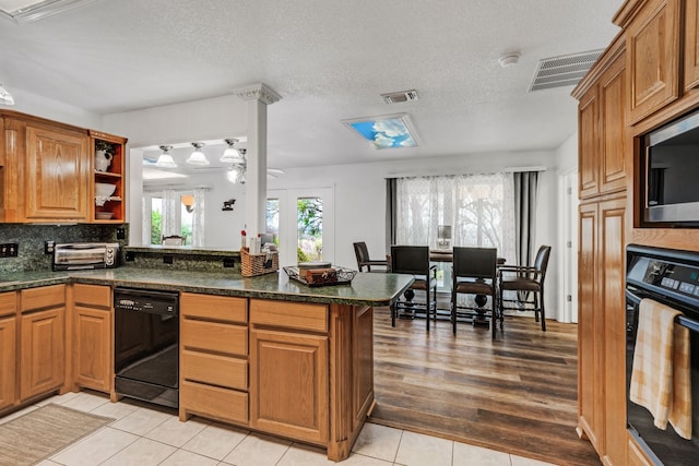 kitchen with brown cabinets, visible vents, a peninsula, and black appliances