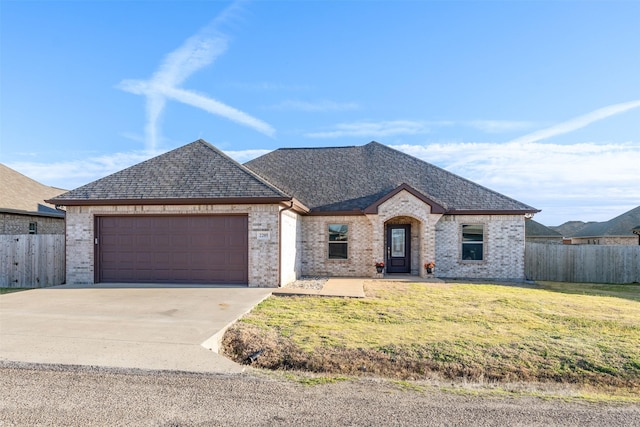 french country home featuring a garage, brick siding, a front yard, and fence