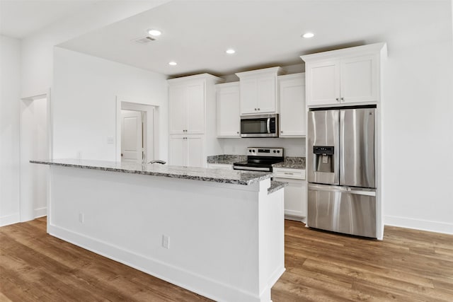 kitchen with light wood finished floors, white cabinets, light stone counters, stainless steel appliances, and recessed lighting