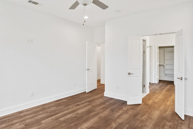 unfurnished bedroom featuring visible vents, a spacious closet, ceiling fan, wood finished floors, and baseboards