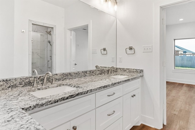 bathroom featuring a marble finish shower, baseboards, a sink, and wood finished floors