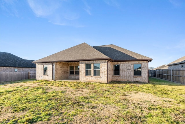 rear view of house featuring brick siding, a fenced backyard, roof with shingles, and a yard