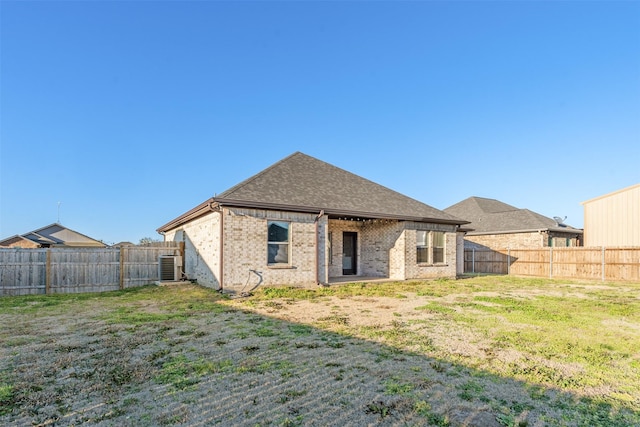 back of property featuring central AC unit, a fenced backyard, brick siding, a yard, and roof with shingles