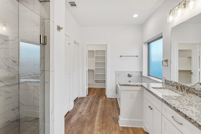 full bathroom featuring wood finished floors, vanity, visible vents, a stall shower, and a walk in closet