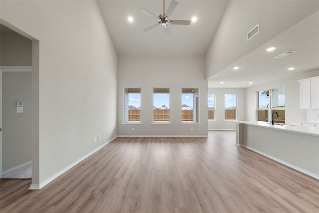 unfurnished living room with light wood-style floors, baseboards, a high ceiling, and visible vents