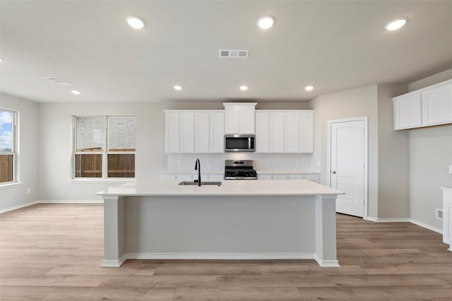 kitchen with visible vents, a kitchen island with sink, stainless steel appliances, light countertops, and a sink