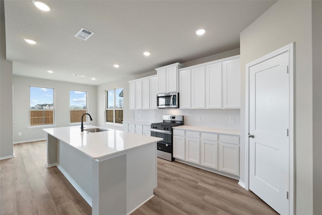 kitchen with tasteful backsplash, appliances with stainless steel finishes, light wood-style floors, a sink, and an island with sink