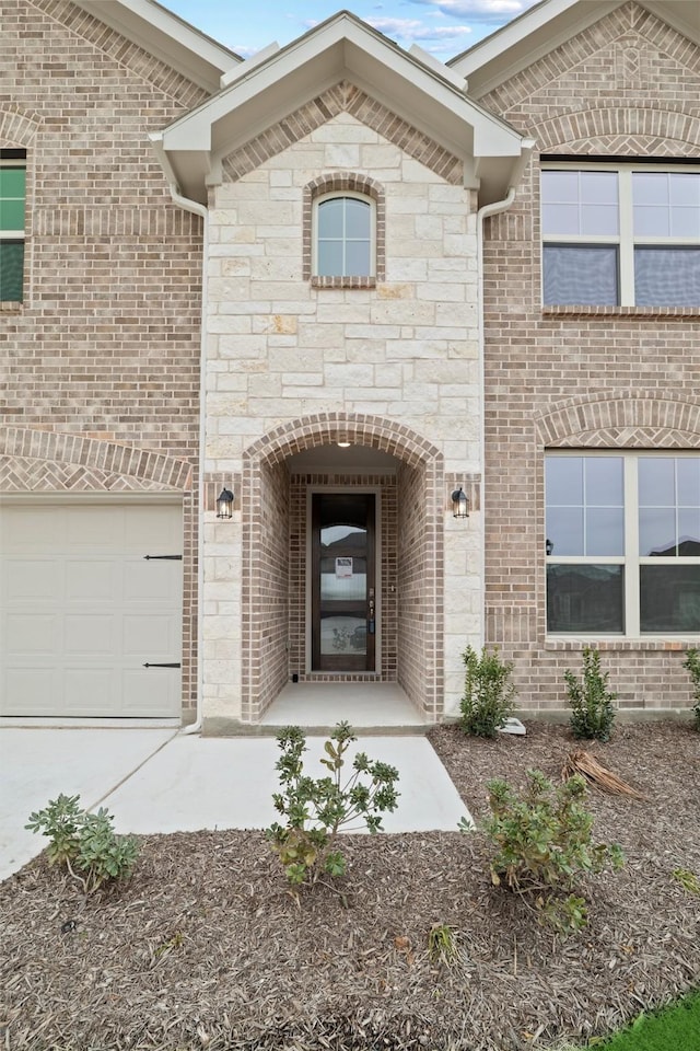 doorway to property with a garage, stone siding, and brick siding