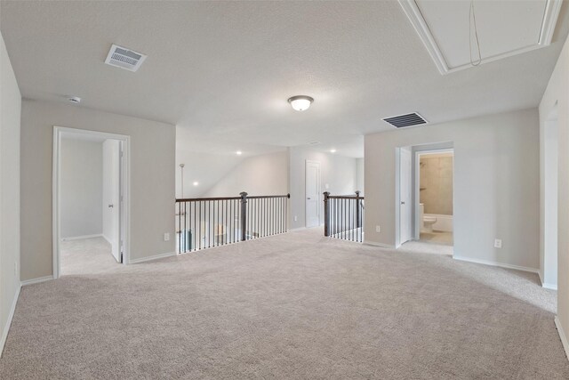 spare room featuring a textured ceiling, light carpet, visible vents, baseboards, and attic access