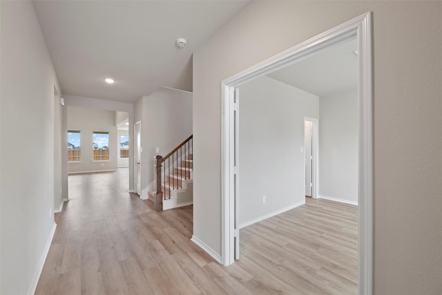 corridor with light wood-type flooring, stairs, and baseboards