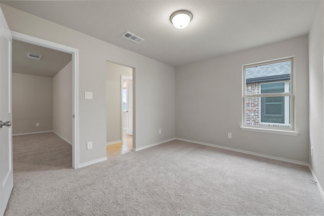 unfurnished bedroom featuring visible vents, light carpet, baseboards, and a textured ceiling