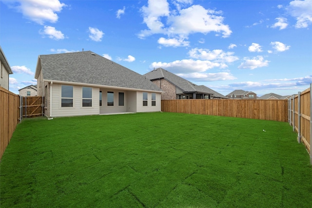 rear view of property featuring a fenced backyard, a lawn, and roof with shingles