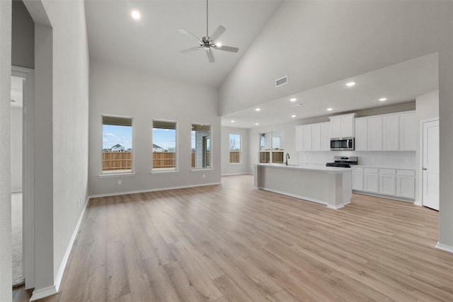 unfurnished living room with light wood-type flooring, high vaulted ceiling, baseboards, and visible vents