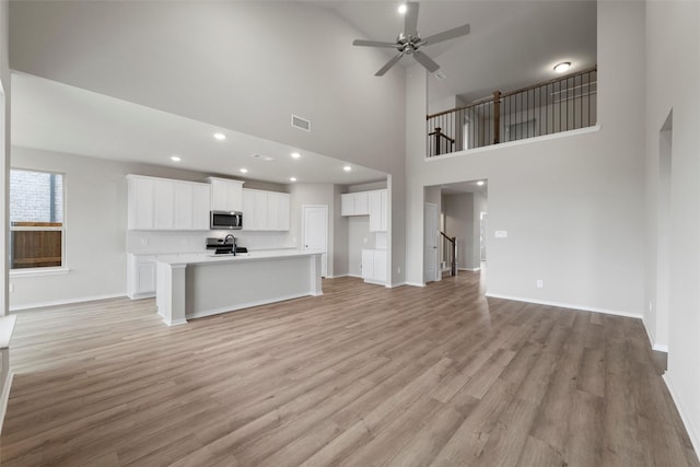 unfurnished living room featuring stairs, ceiling fan, light wood finished floors, and baseboards