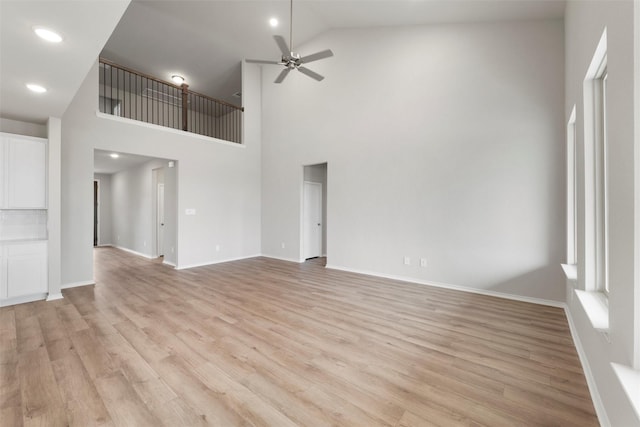 unfurnished living room with ceiling fan, high vaulted ceiling, light wood-style flooring, and baseboards