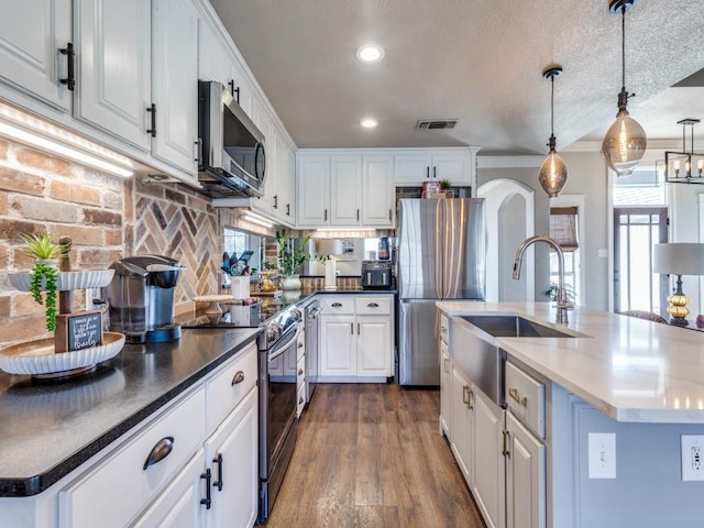 kitchen featuring arched walkways, wood finished floors, stainless steel appliances, white cabinetry, and a sink