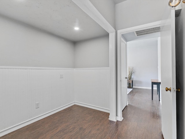 hallway with a wainscoted wall, visible vents, and dark wood finished floors