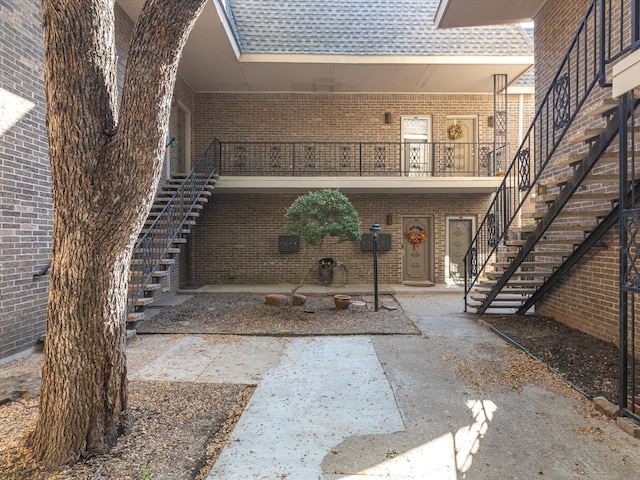 doorway to property with a shingled roof, brick siding, and a patio