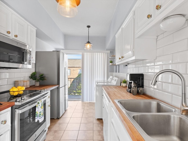 kitchen featuring white cabinets, wood counters, stainless steel appliances, washer and dryer, and a sink