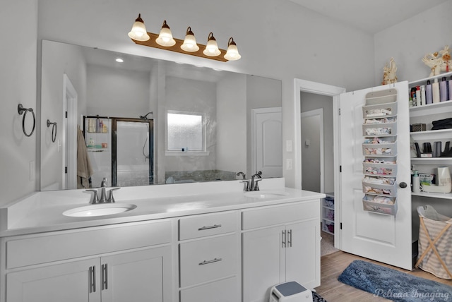 full bath with double vanity, a sink, a shower stall, and wood finished floors