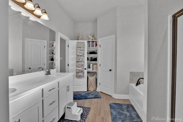 full bath with a garden tub, double vanity, wood finished floors, and a sink