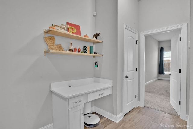 interior space featuring light wood finished floors, built in study area, and baseboards