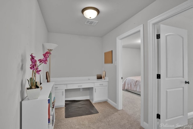 interior space featuring light carpet, baseboards, visible vents, and built in desk