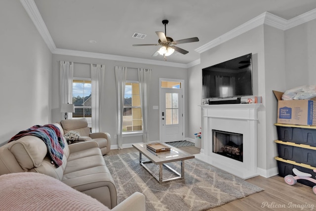 living area with baseboards, visible vents, ceiling fan, wood finished floors, and crown molding