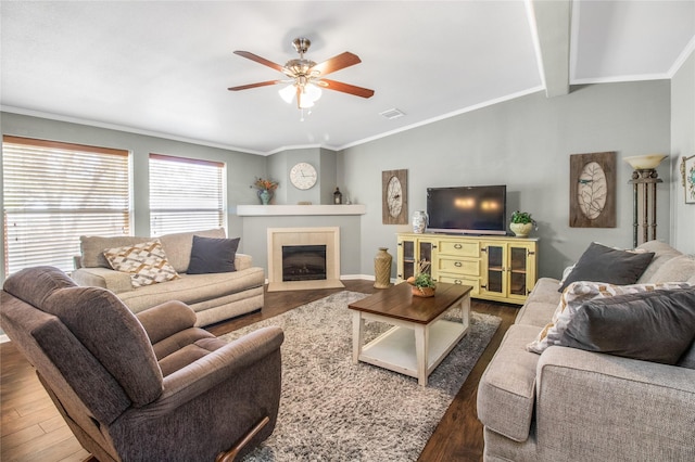 living room featuring wood finished floors, visible vents, vaulted ceiling, a tiled fireplace, and crown molding