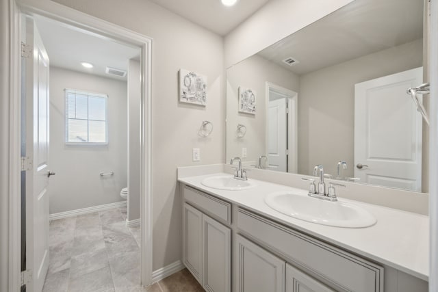 bathroom with visible vents, double vanity, a sink, and toilet