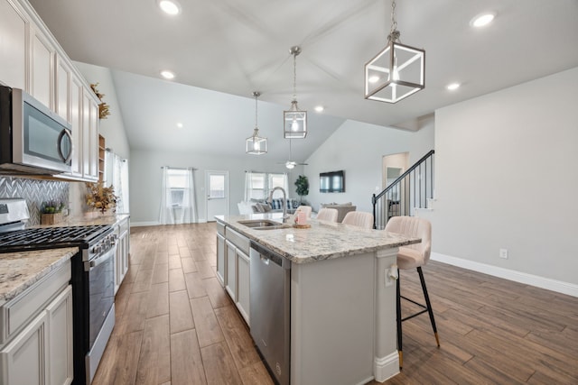 kitchen with a kitchen island with sink, dark wood-type flooring, a breakfast bar, a sink, and appliances with stainless steel finishes