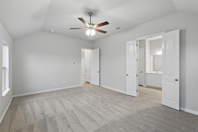 unfurnished bedroom with visible vents, baseboards, light colored carpet, ensuite bath, and vaulted ceiling