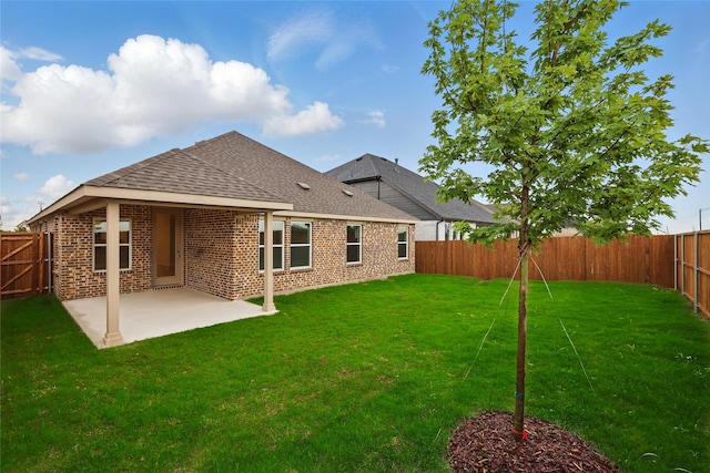 rear view of house with a patio area, brick siding, a fenced backyard, a lawn, and a shingled roof