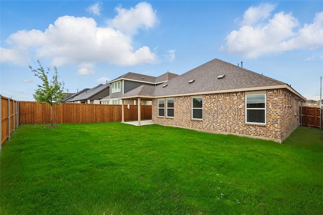 rear view of property featuring a yard, brick siding, roof with shingles, and a fenced backyard