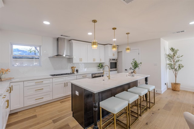 kitchen featuring wall chimney range hood, light wood-style flooring, cooktop, and visible vents